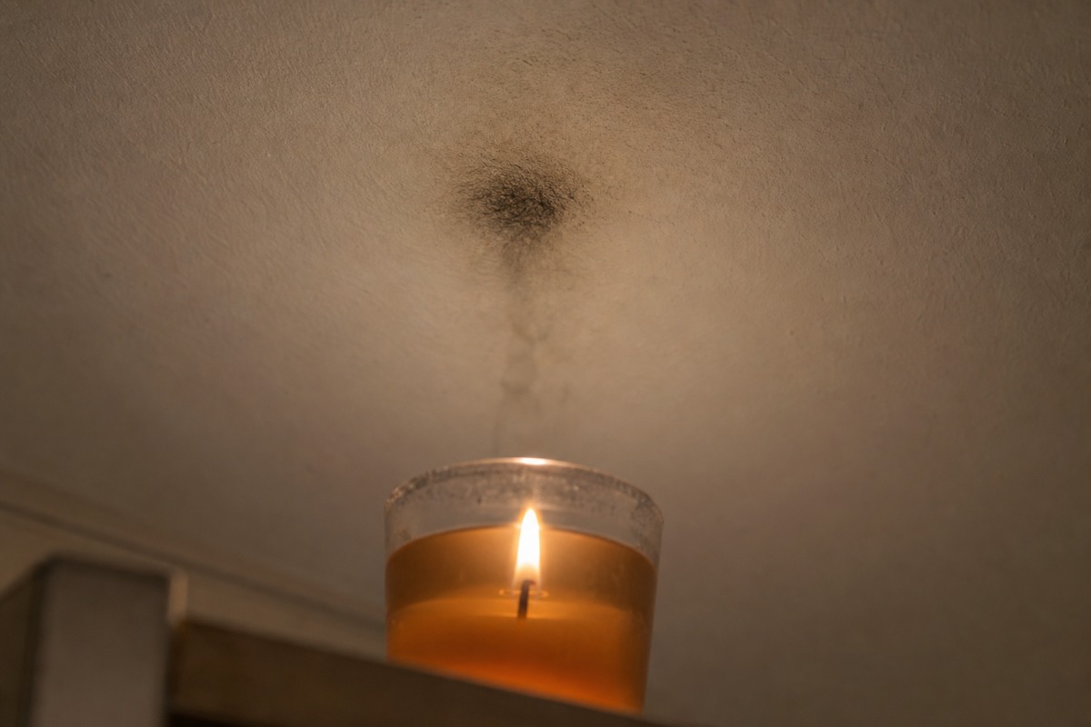 Dunkle Rußspur an einer weißen Decke direkt über einer brennenden Gelkerze im Glas